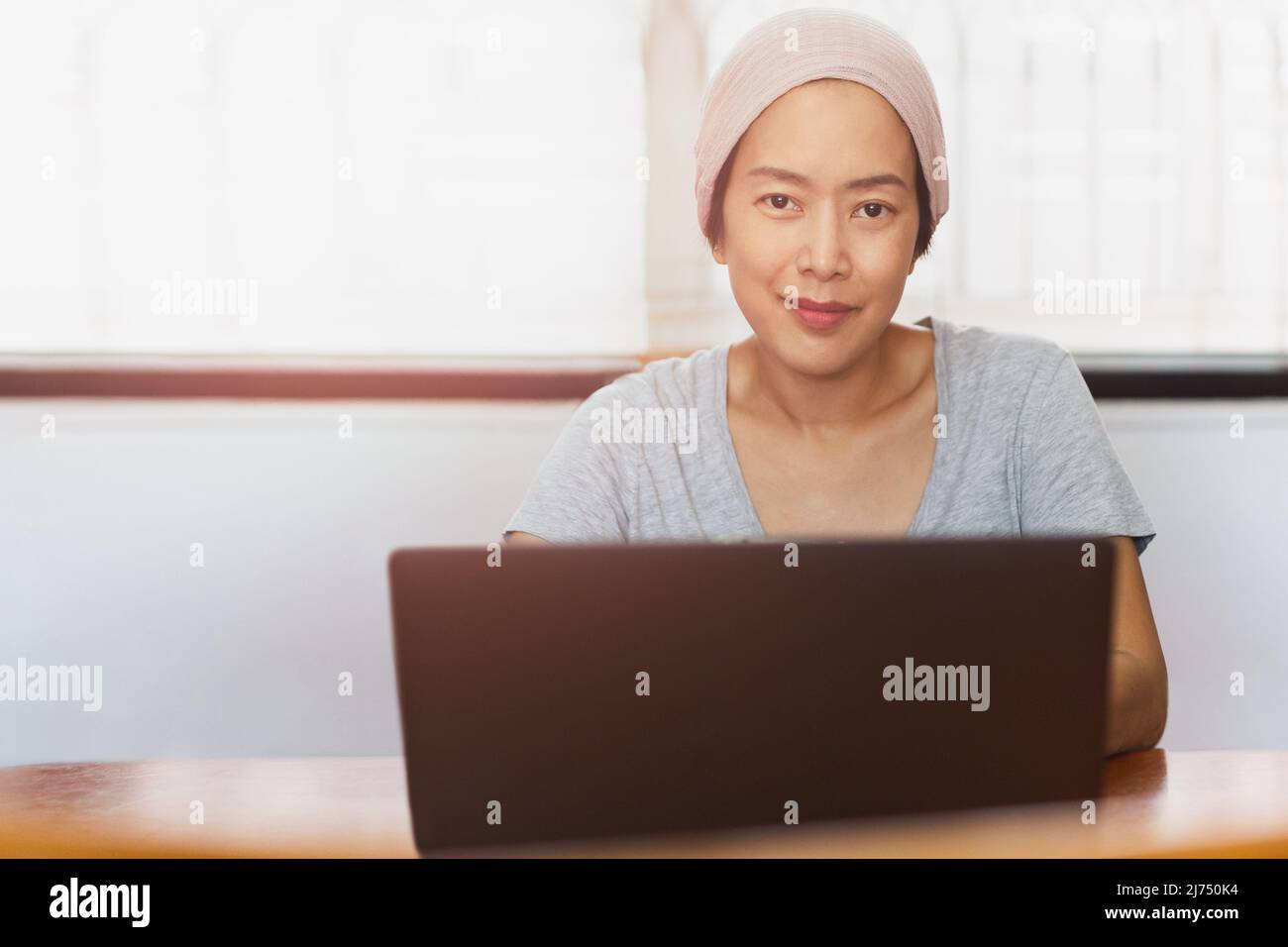 Donna che indossa un cappello di lana che lavora su un computer portatile e guarda la fotocamera a casa. Foto Stock