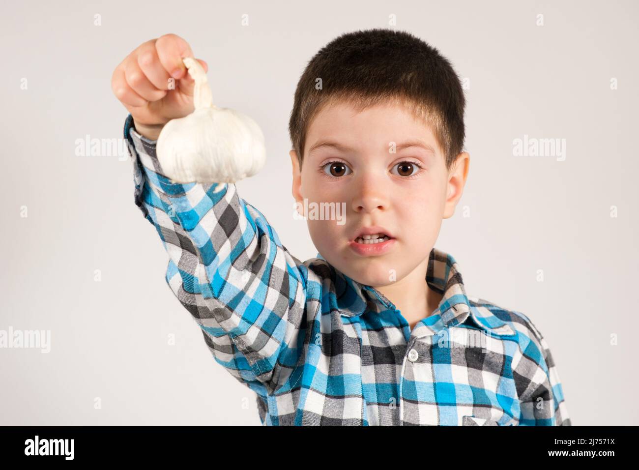 Un ragazzo di 4 anni di età prescolare tiene l'aglio e guarda nella fotocamera su uno sfondo bianco. Verdure e vitamine per i bambini. Foto Stock