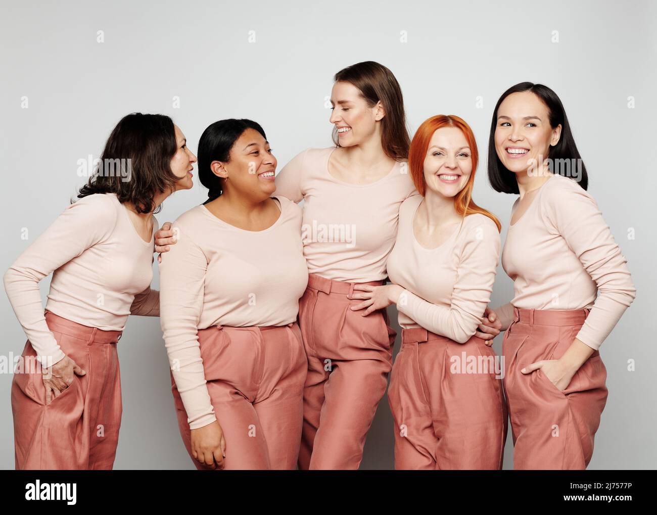 Gruppo di donne interrazziali positive negli stessi vestiti che si abbracciano e ridono insieme Foto Stock