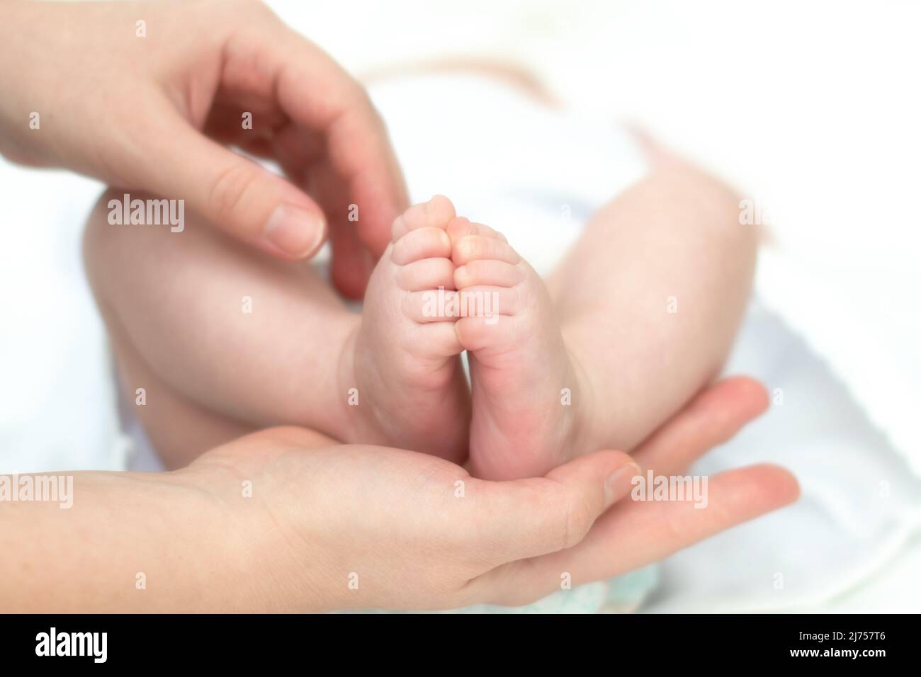 Le mani della madre tengono teneramente e con amore le gambe di un bambino piccolo che ha diversi mesi dal momento della nascita. Foto Stock