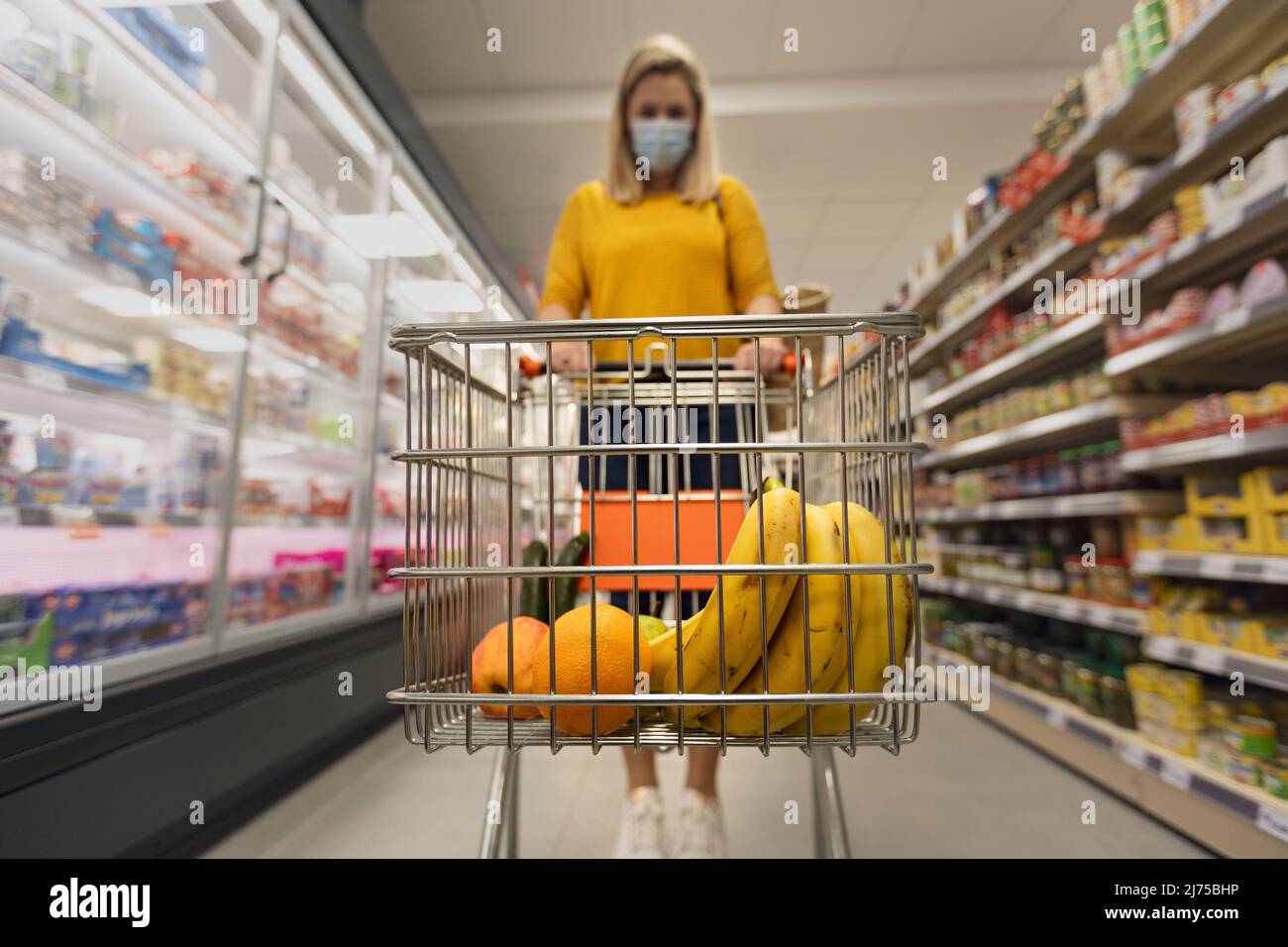 Giovane donna in maschera con carrello shopping in supermercato, concetto di inflazione. Foto Stock