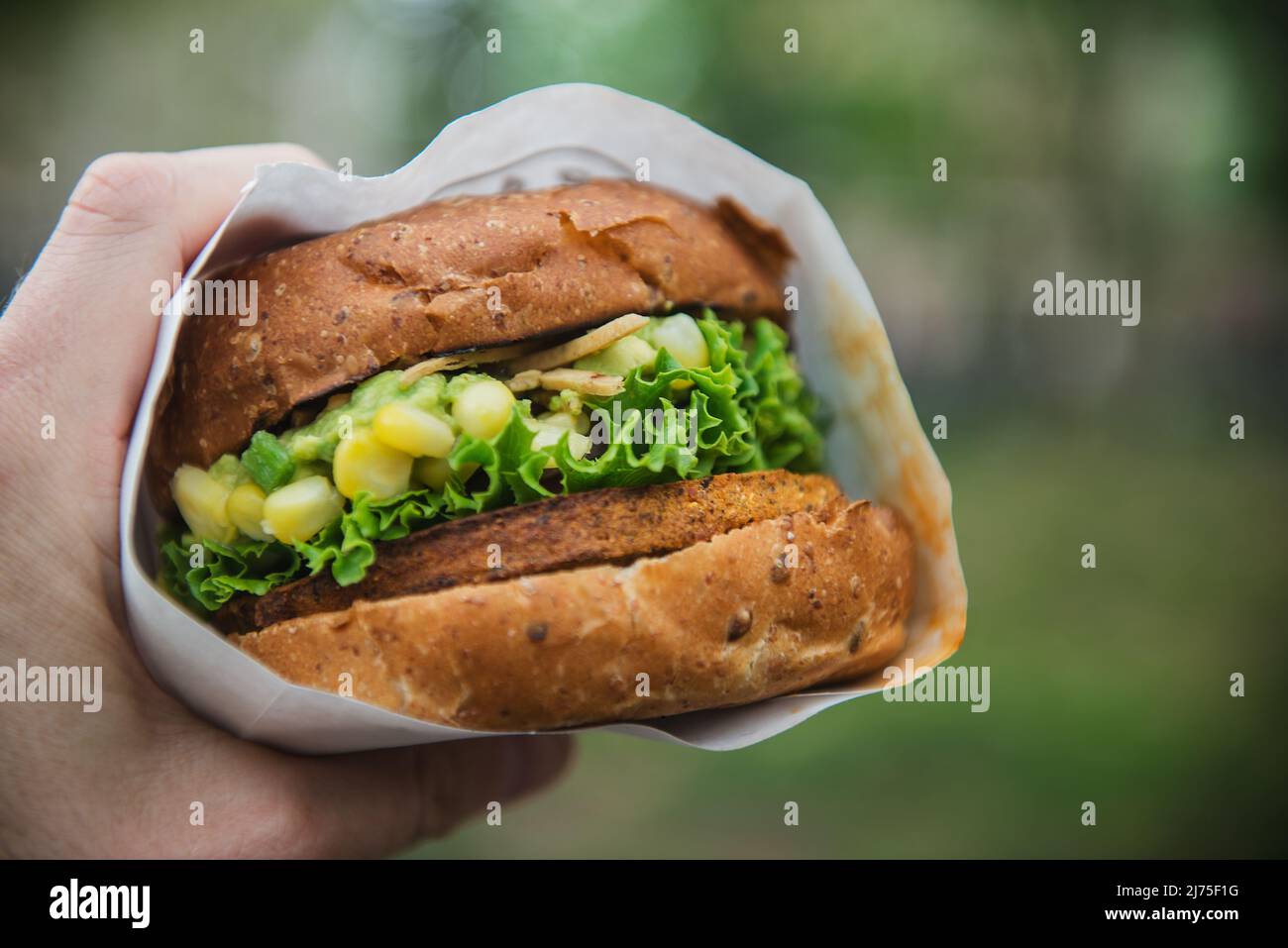 Una mano che tiene un hamburger vegetariano con mais, lattuga e guacamole Foto Stock