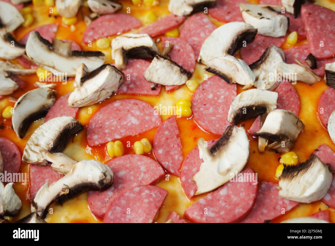 Defocalizzare gli ingredienti del primo piano per la pizza sull'impasto. Salsa di pomodoro rosso, salsicce, mais dolce. Pizza italiana fatta in casa. Base di Margarita. Home culinario. Superiore Foto Stock