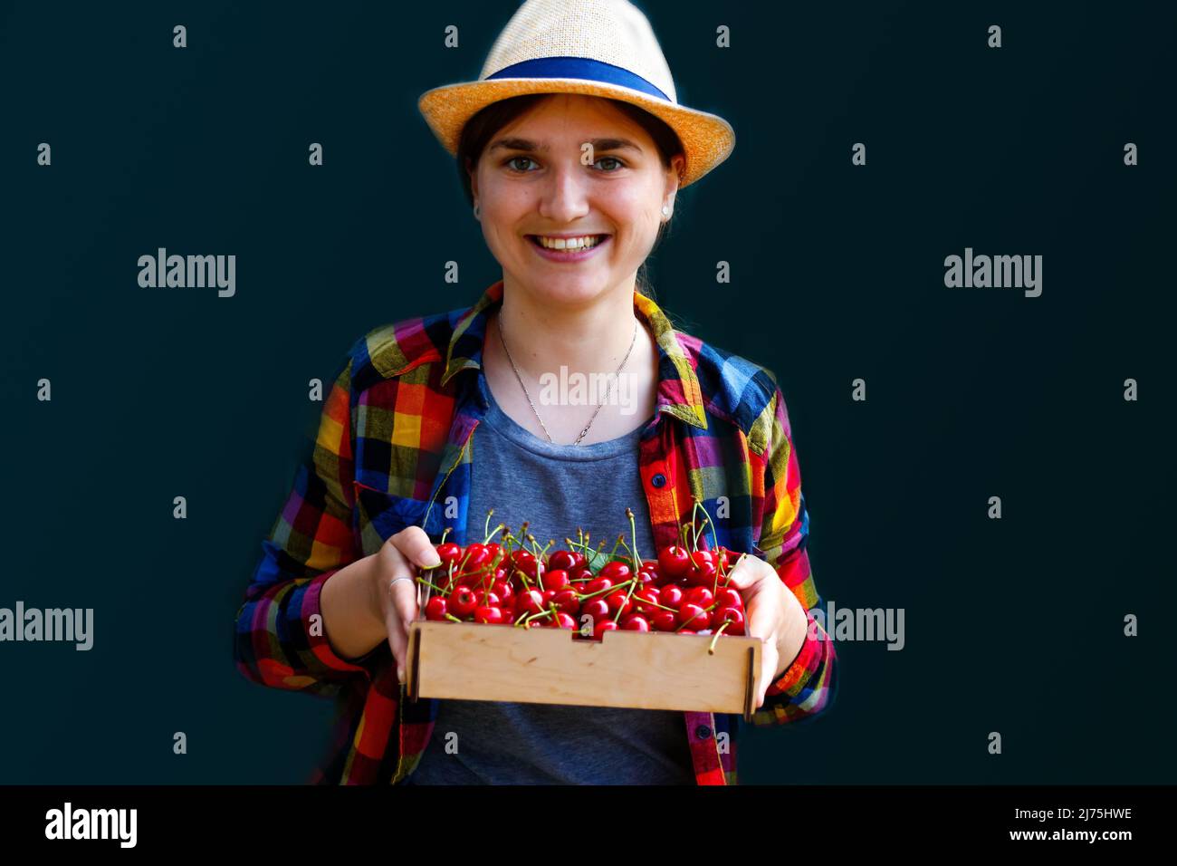 Sfocare la giovane donna in un cappello e una camicia sorride e mostra un  cestino di ciliegie e ciliegie dolci. Sfondo verde scuro. Cibo estivo,  frutta. Estate Foto stock - Alamy