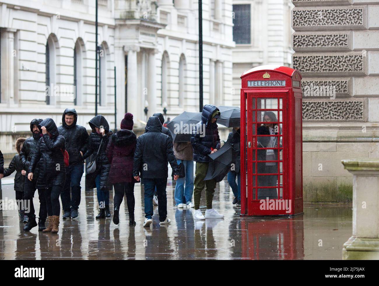 Le persone con ombrelloni si riuniscono intorno a una cassetta telefonica rossa a Westminster, nel centro di Londra. Foto Stock