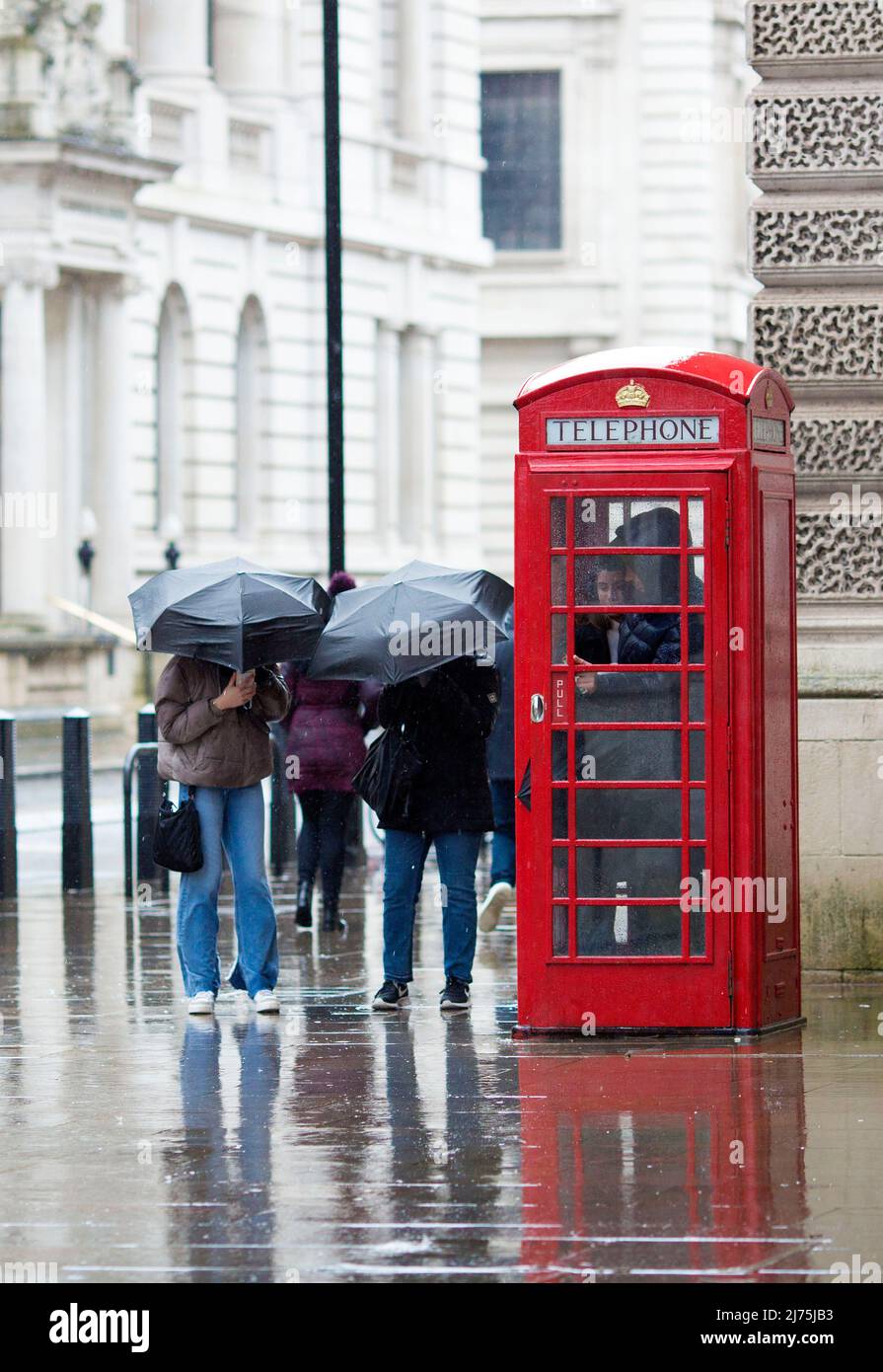 Le persone con ombrelloni si riuniscono intorno a una cassetta telefonica rossa a Westminster, nel centro di Londra. Foto Stock