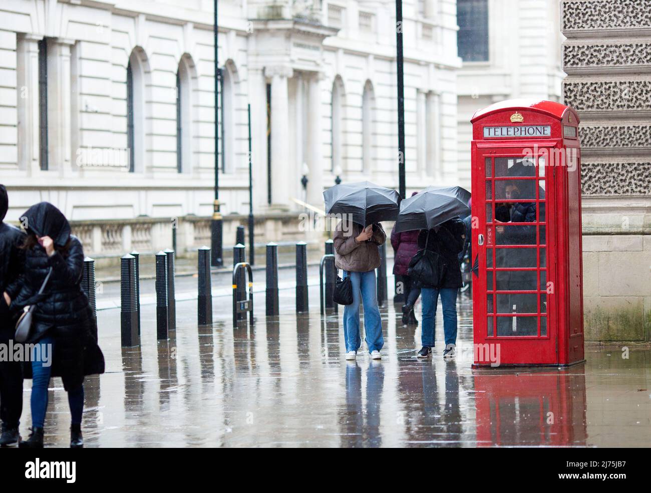 Le persone con ombrelloni si riuniscono intorno a una cassetta telefonica rossa a Westminster, nel centro di Londra. Foto Stock