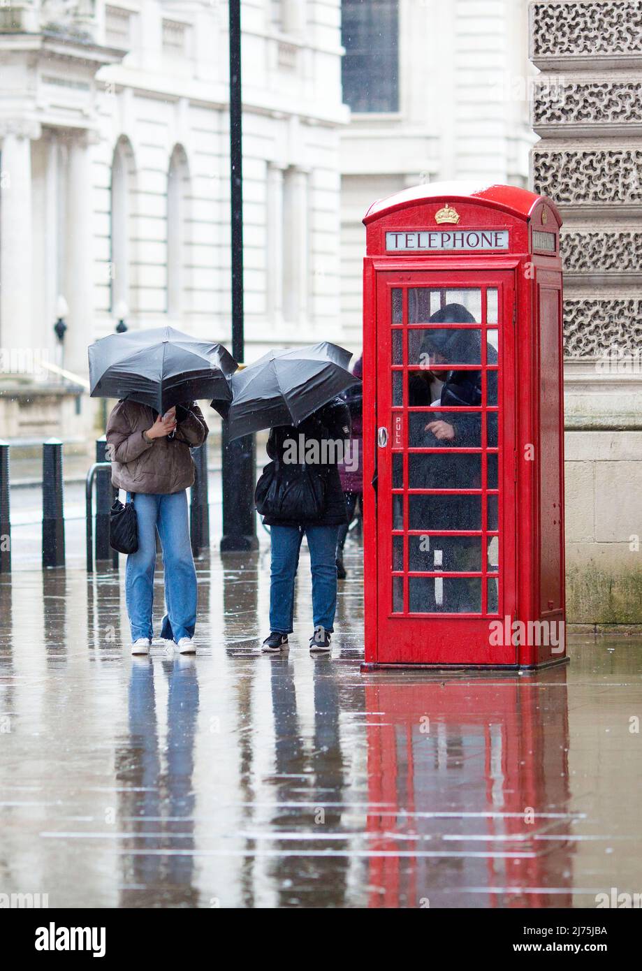 Le persone con ombrelloni si riuniscono intorno a una cassetta telefonica rossa a Westminster, nel centro di Londra. Foto Stock