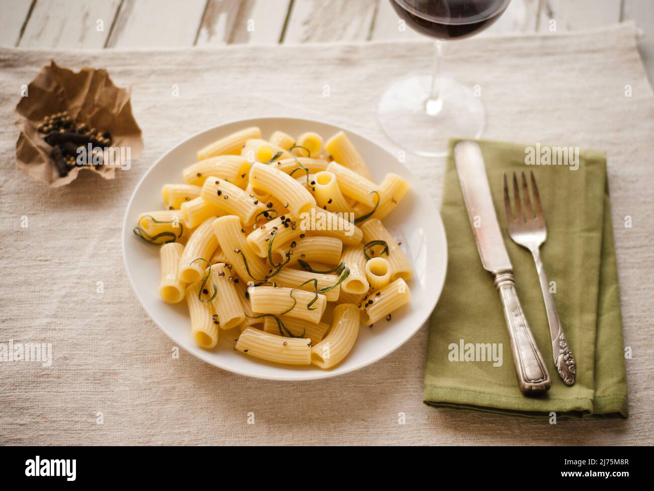 Rigatoni con olio d'oliva, pepe ed erbe fresche; bicchiere di vino rosso a forchetta e coltello Foto Stock