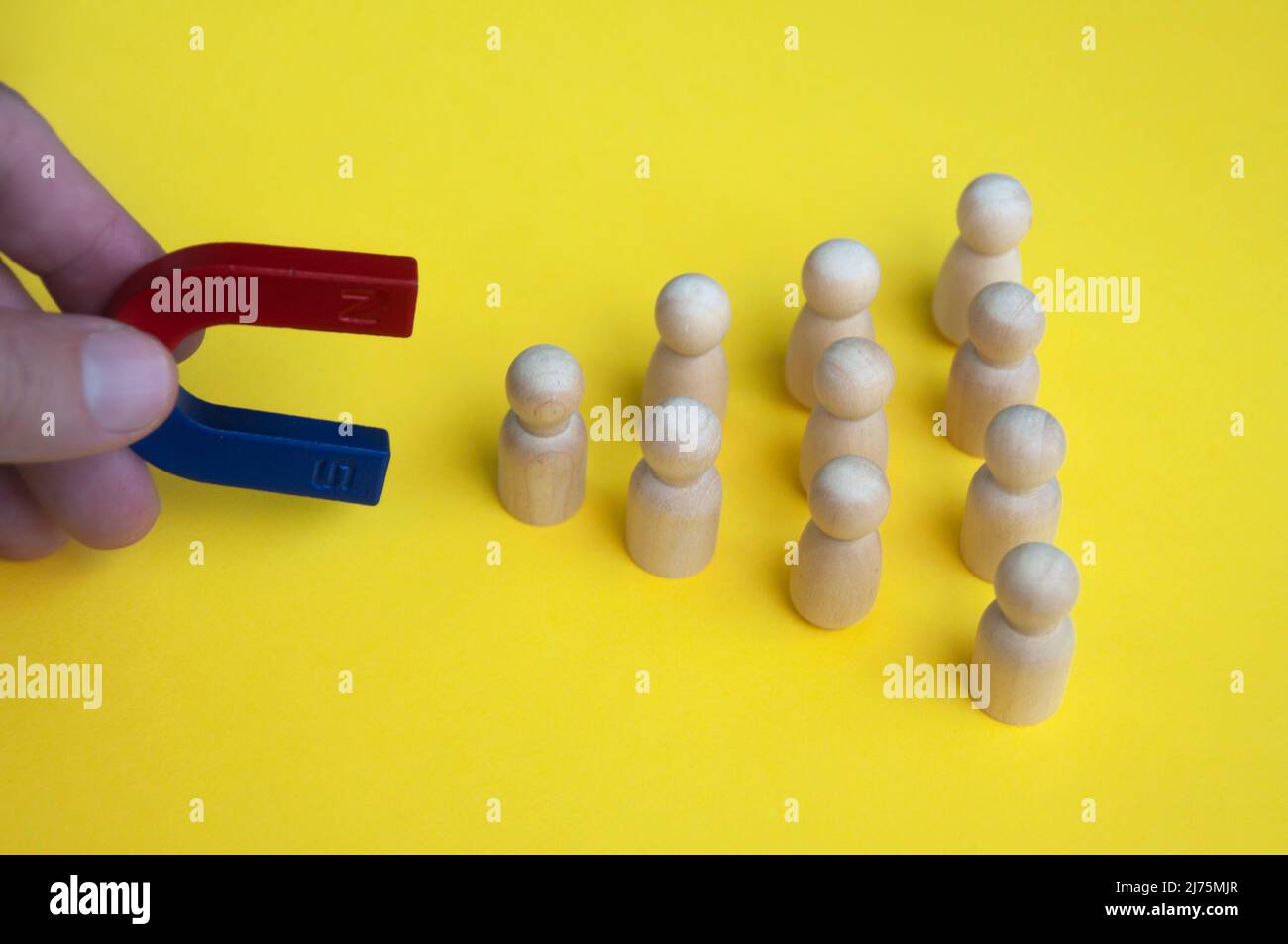 Magnete di tenuta a mano che attrae bambole di legno su sfondo giallo. Concetto di legge dell'attrazione. Foto Stock