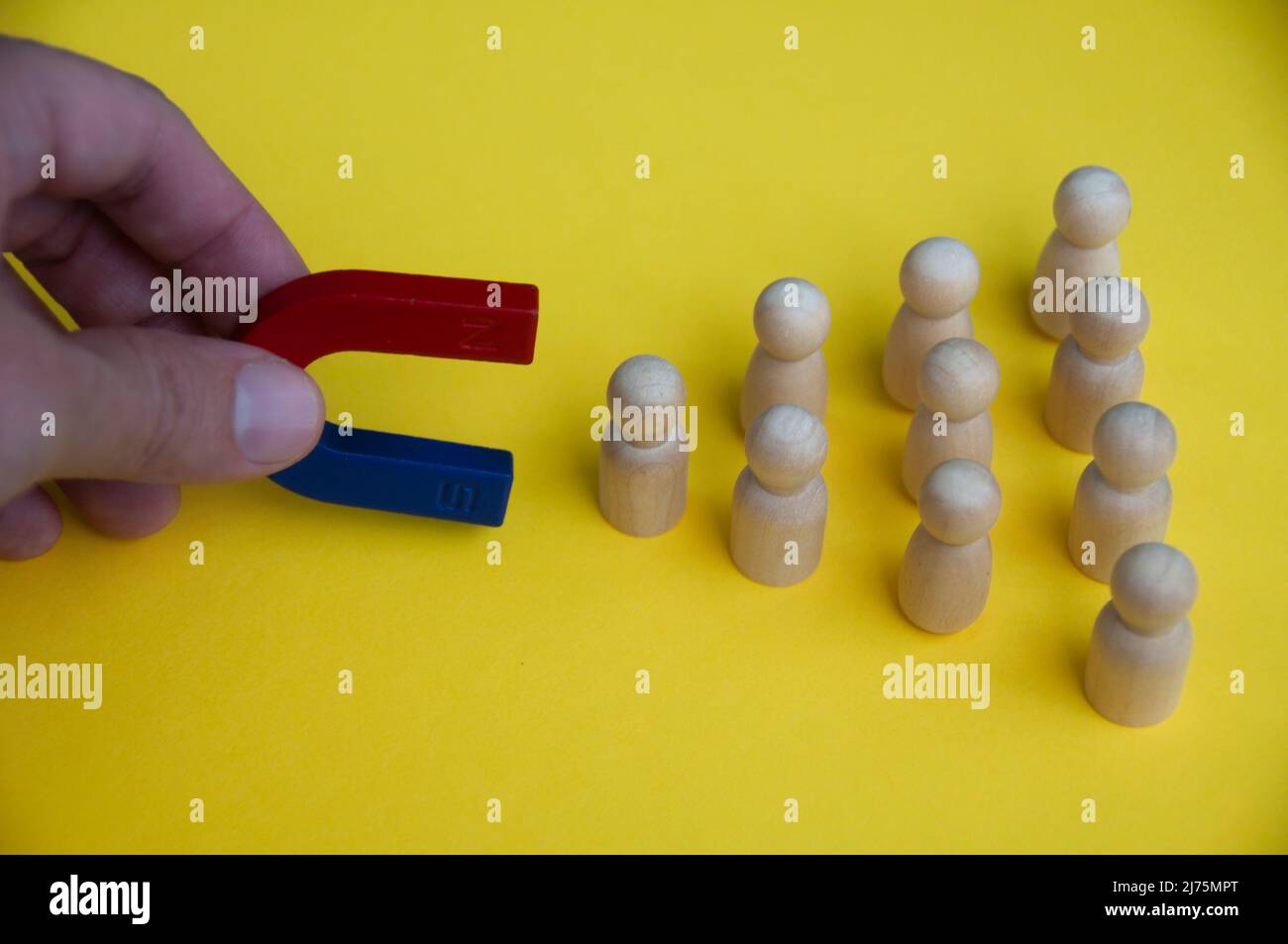 Magnete di tenuta a mano che attrae bambole di legno su sfondo giallo. Concetto di legge dell'attrazione. Foto Stock