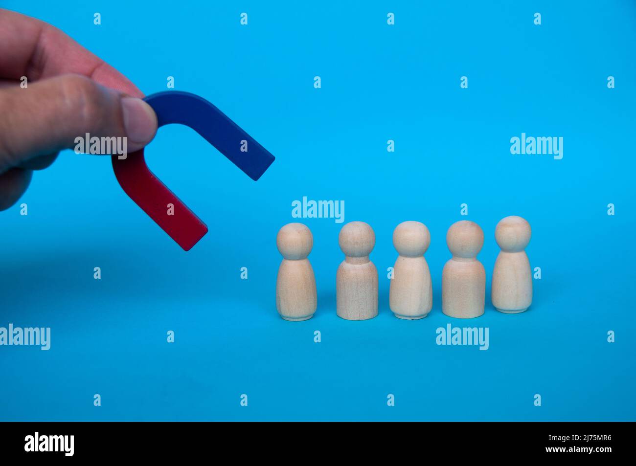 Magnete di tenuta a mano che attrae bambole di legno su sfondo blu. Concetto di legge dell'attrazione. Foto Stock