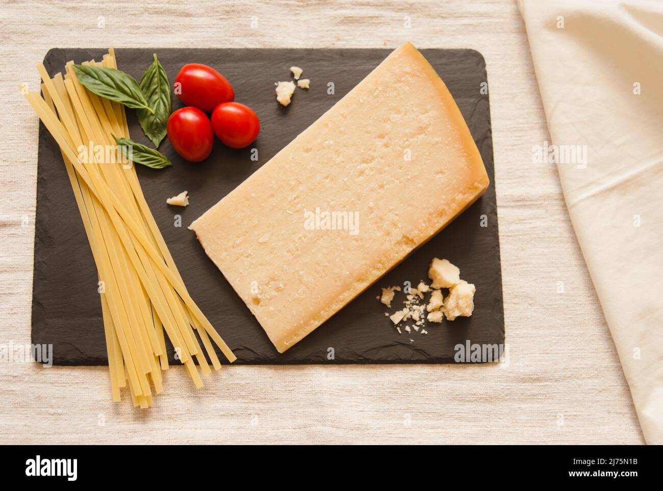 Un cuneo di parmigiano con pasta secca, pomodori e basilico su ardesia Foto Stock