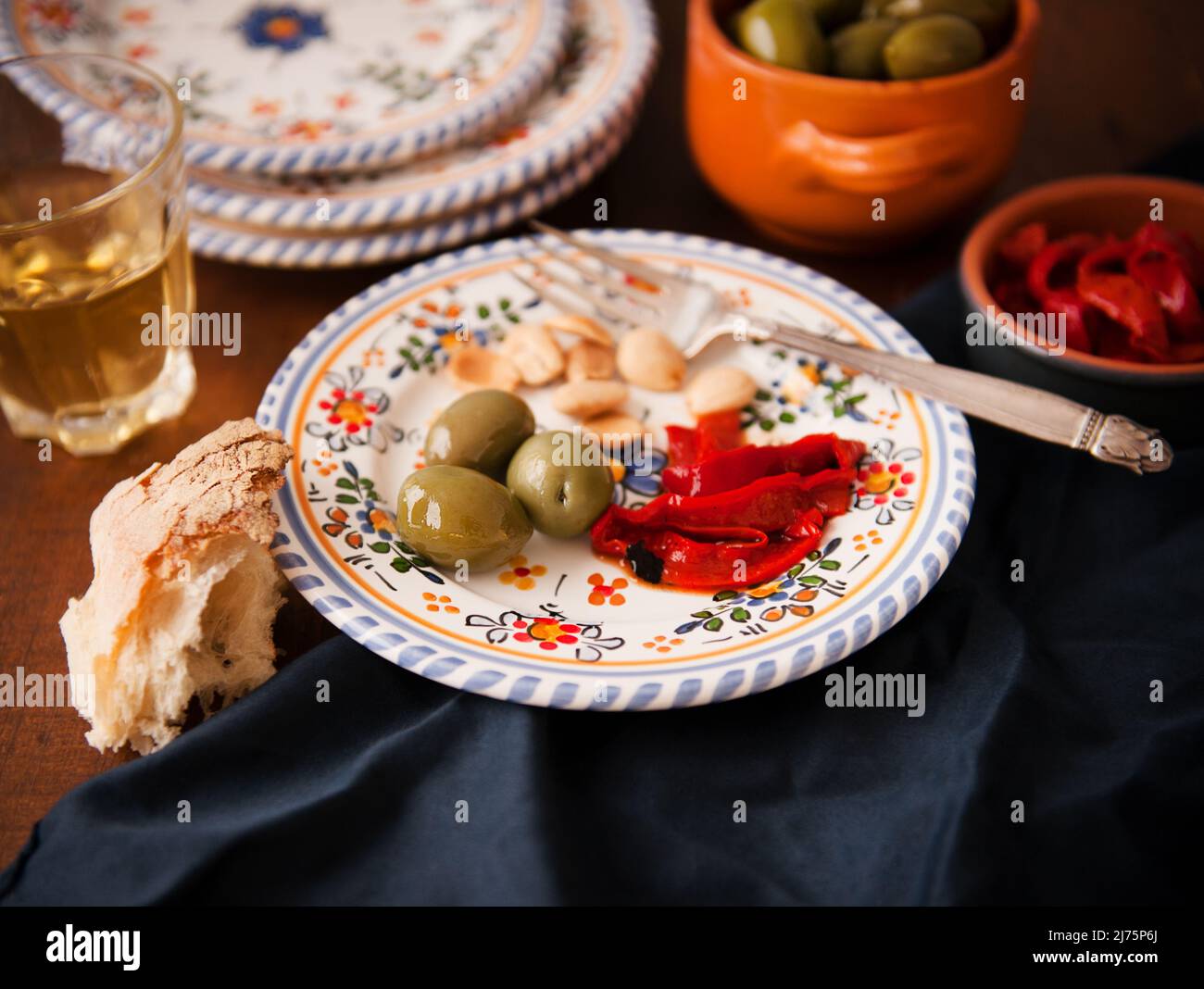 Piatto con una sola porzione di tapas; olive verdi, peperoni rossi arrostiti e mandorle; pane e vino bianco Foto Stock