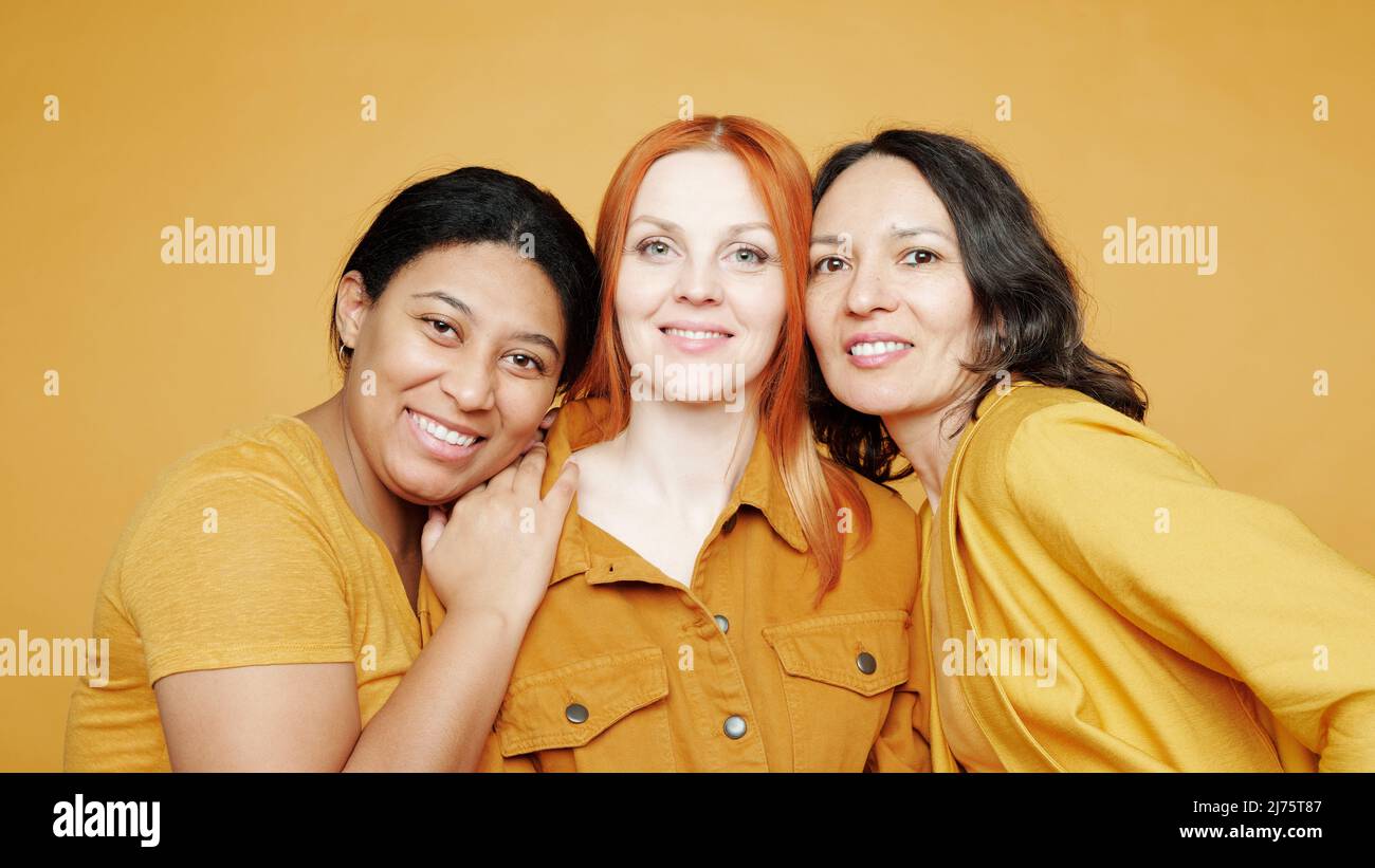 Gruppo di amici positivi multietnici di sesso femminile completamente diversi l'uno dall'altro posando su sfondo giallo Foto Stock