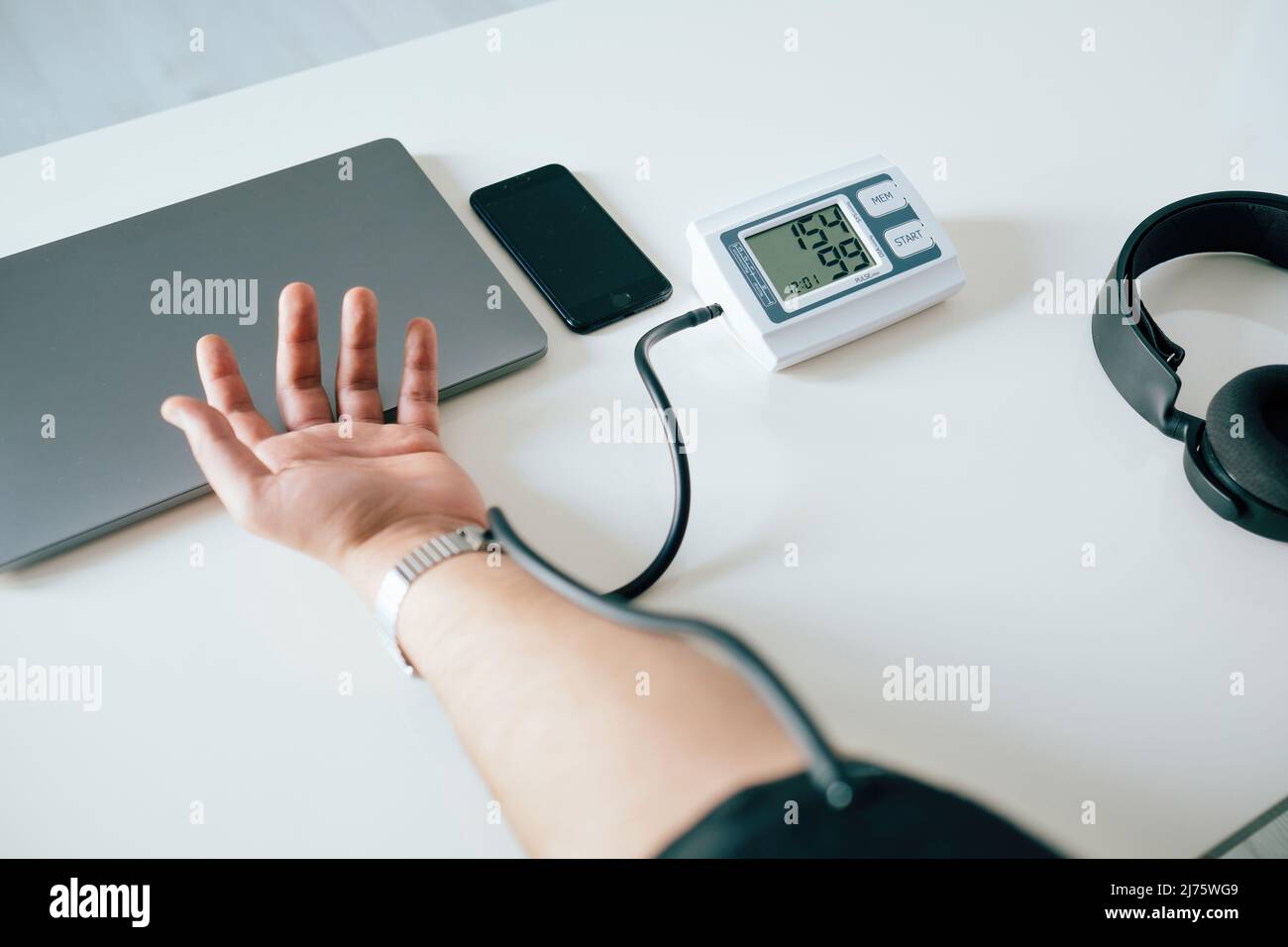 Pressione sanguigna, giovane uomo che indossa un bendaggio per la pressione sanguigna sul braccio e controlla il ritmo cardiaco, il consumo eccessivo di caffè e l'intenso lavoro TEM Foto Stock