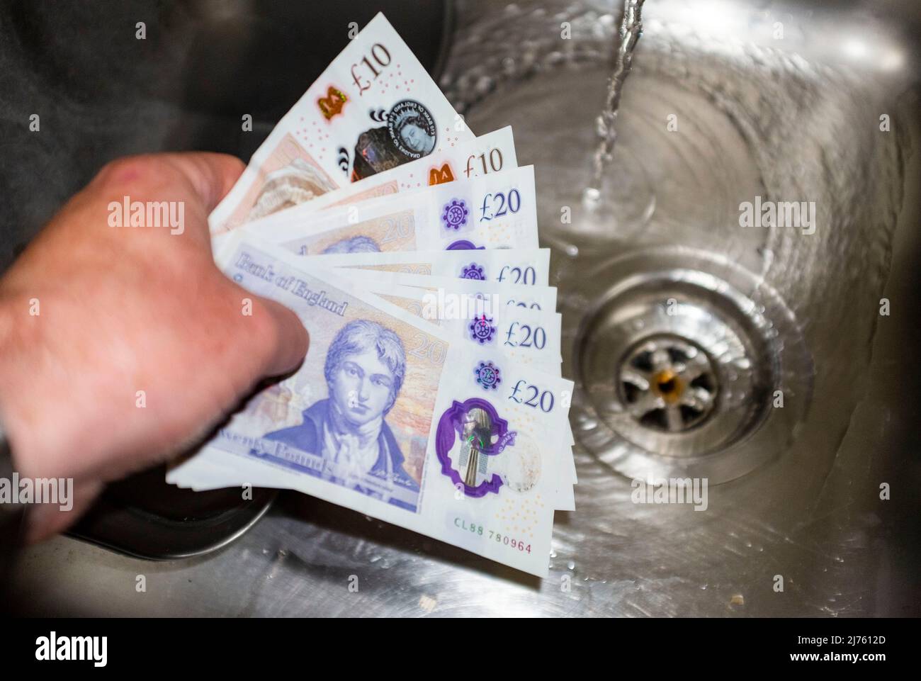 Mani che tengono £20 e £10 note per illustrare i contanti in mano e pagare in contanti o gettando soldi giù lo scolo Foto Stock