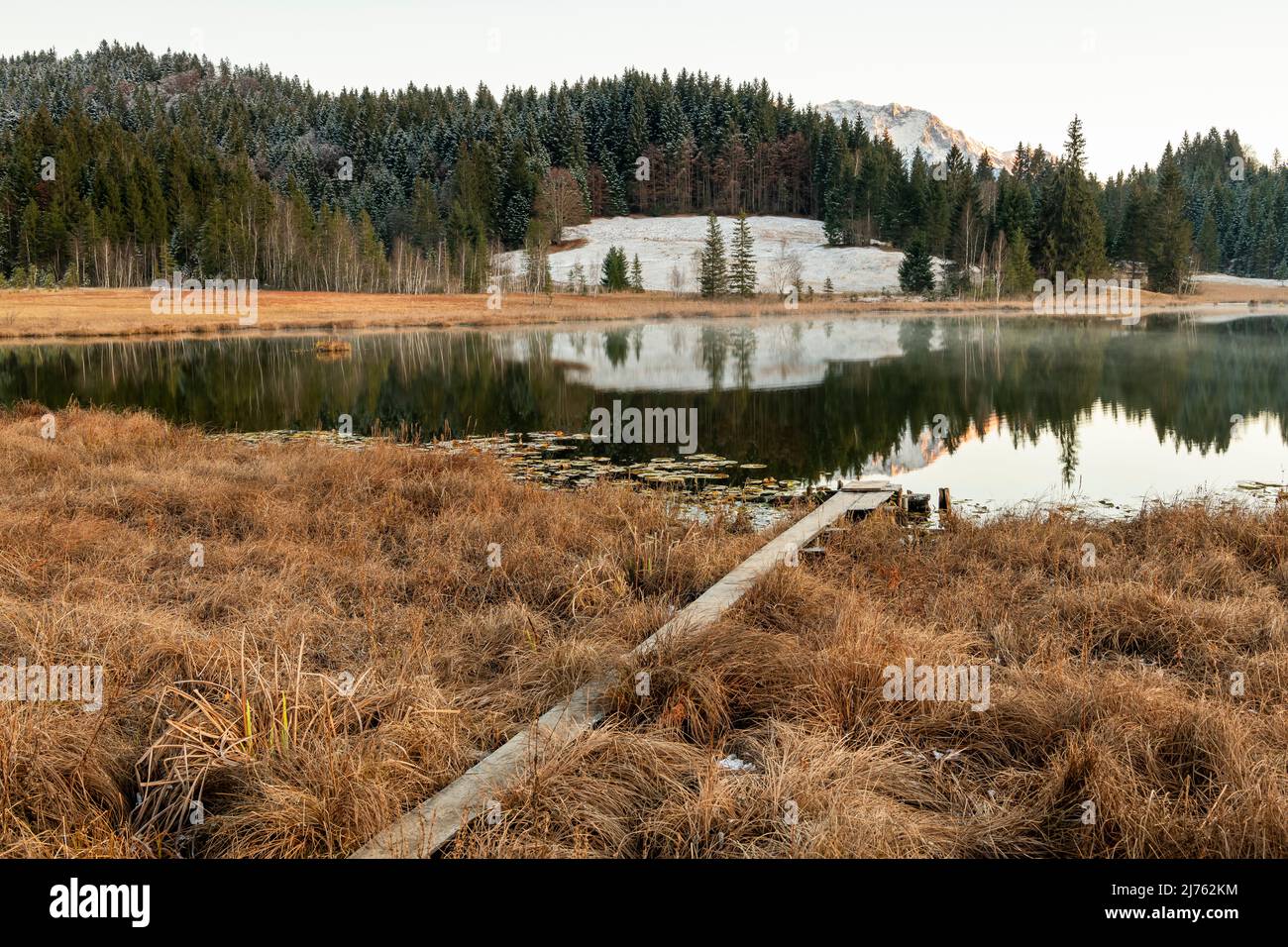 Un freddo pomeriggio autunnale a Geroldsee, chiamato anche Wagenbrüchsee, un ponte pedonale in primo piano, sullo sfondo alcune neve fresca e il Karwendel. Una stretta passerella conduce attraverso le canne al lago di fossato. Foto Stock