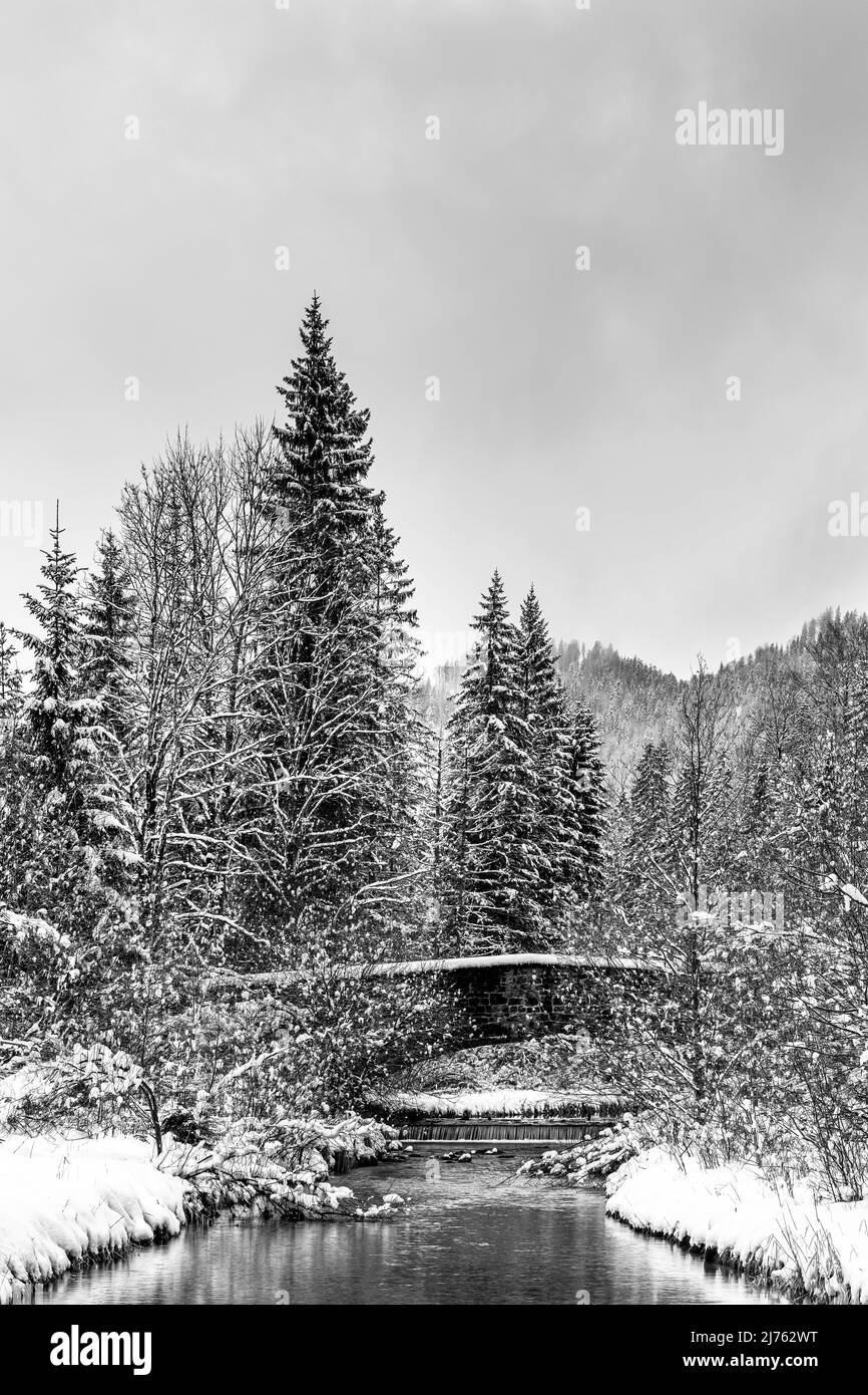 Vecchio ponte in pietra sull'Obernach tra Wallgau e Walchensee in inverno con neve fitta e nuvole. Il piccolo torrente si snoda attraverso il paesaggio invernale Foto Stock