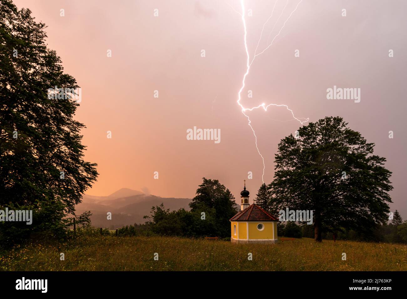 Temporale con fulmine alla piccola cappella Maria Rast in Werdenfelser Land nelle Alpi bavaresi tra Mittenwald e Garmisch Partenkirchen, durante la sera in un'atmosfera rossastra. Foto Stock