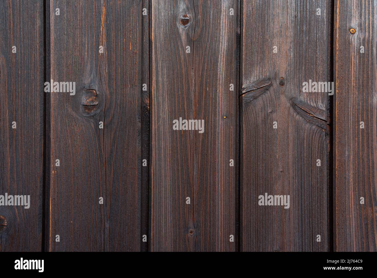 Struttura dettagliata di una parete in legno marrone scuro con tavole verticali. Superficie in legno naturale a grana visibile, nodi e struttura resistente agli agenti atmosferici. Foto Stock