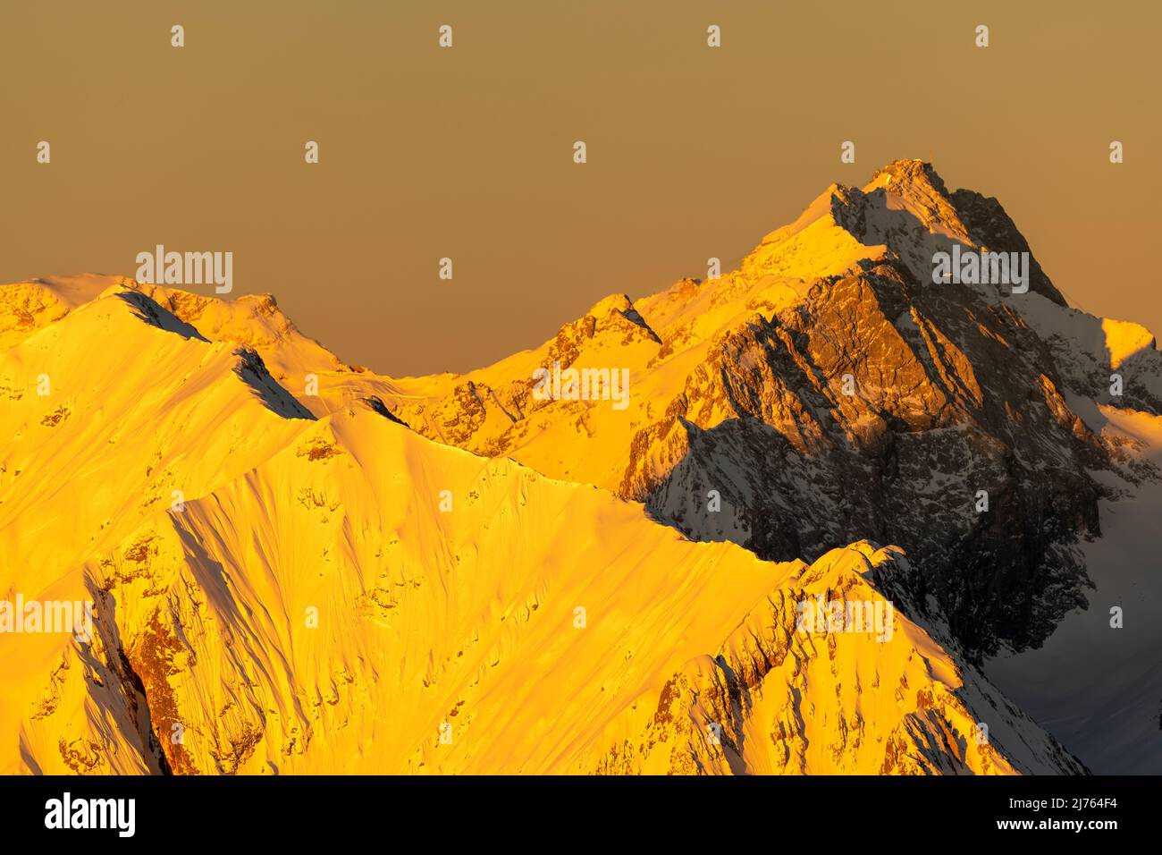 La luce dorata all'alba fa risplendere lo Zugspitze e la cresta di Hochblassen sopra Garmisch-Partenkirchen nelle Alpi tedesche giallo dorato. Vista dal Karwendelspitze occidentale. Foto Stock