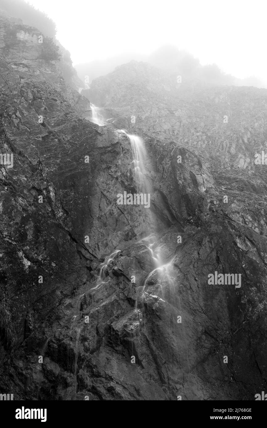 Piccola cascata a Karwendel nelle Alpi nella nebbia. La cascata si trova vicino al Gradai Hochleger nel parco naturale e cade su una parete di roccia impressionante. Foto Stock