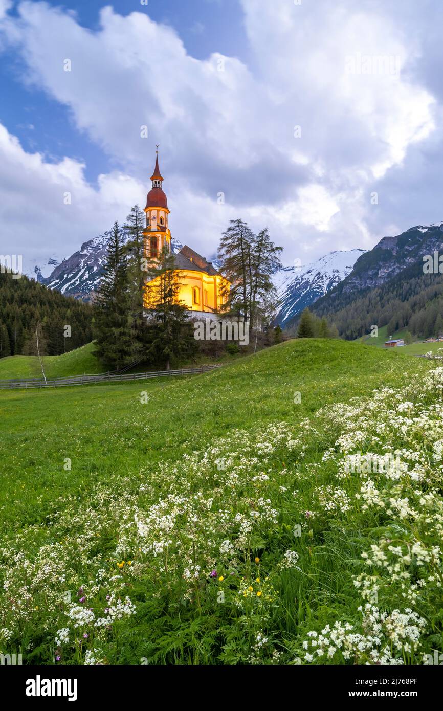 Vecchi mulini di legno a Obernberg am Brenner, la chiesa storica di San Nicola sullo sfondo e prati fioriti in primo piano. Foto Stock
