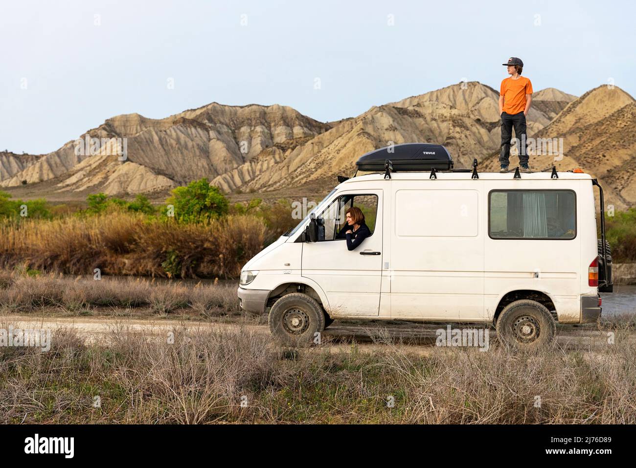 Madre seduta e figlio in piedi sulla cima di camper van in arido paesaggio e montagne rocciose, Vashlovani parco nazionale, Georgia Foto Stock