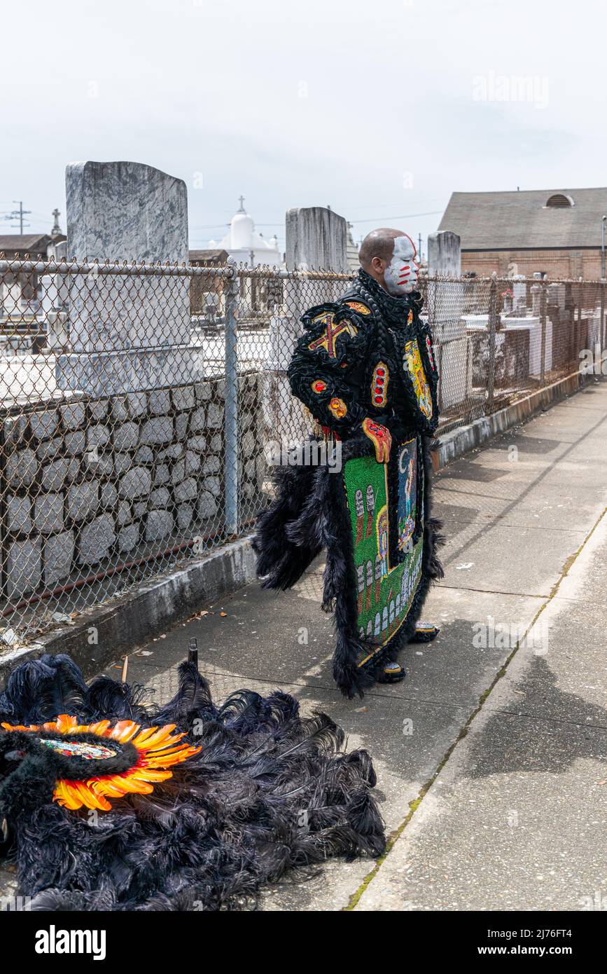 NEW ORLEANS, LA, USA - 17 MARZO 2019: Uomo in nero Mardi Gras costume indiano con headdress sul terreno si ferma sul marciapiede di fronte al cimitero Foto Stock