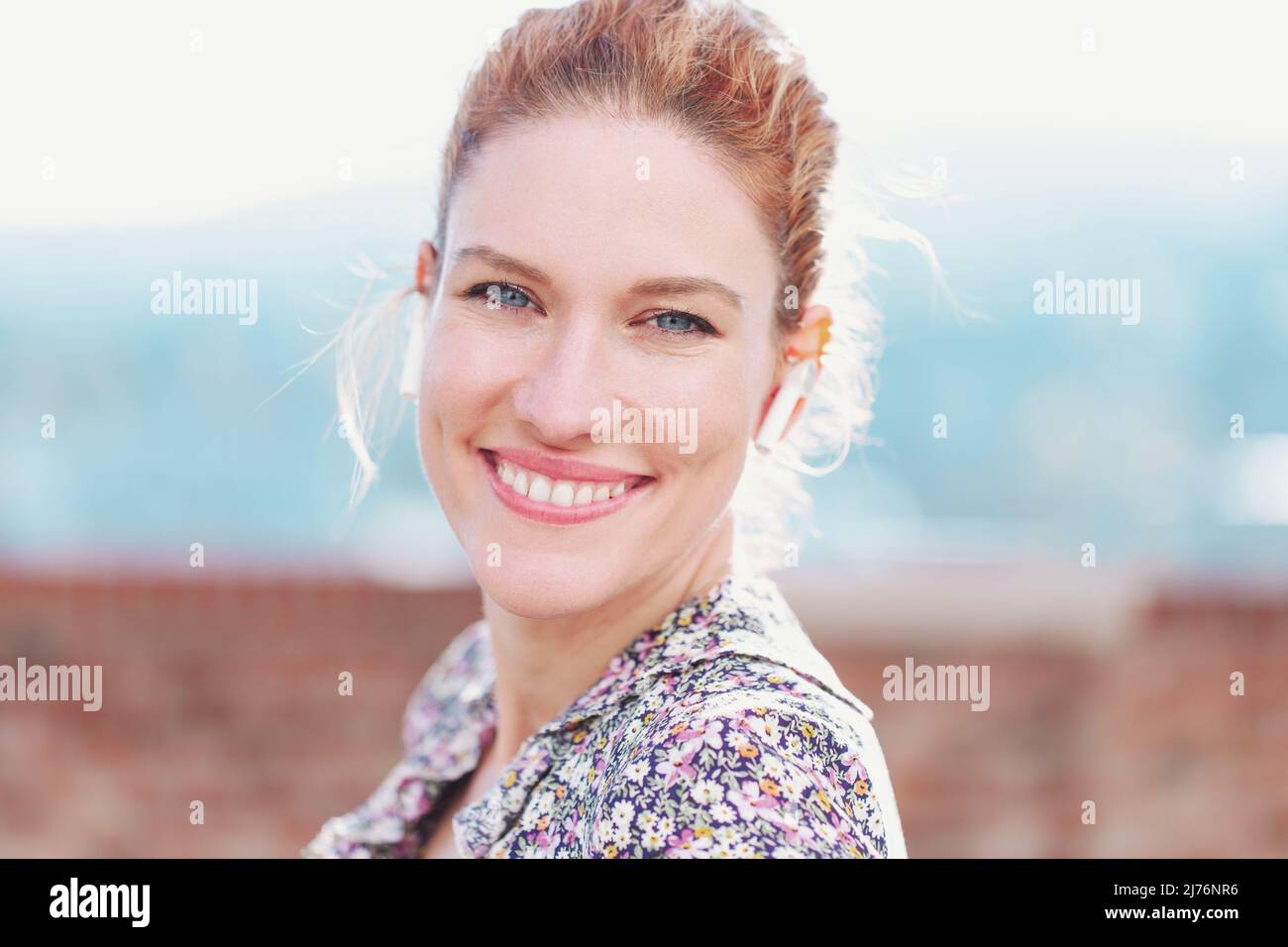 Giovane ragazza allegra rossa con dispositivo a mani libere che sorride all'aperto Foto Stock