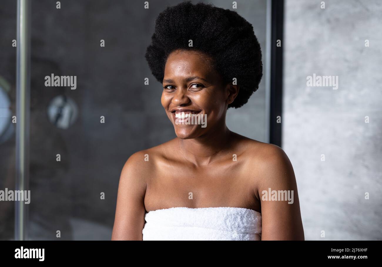 Ritratto di felice afroamericana metà adulta donna avvolto in asciugamano a casa Foto Stock
