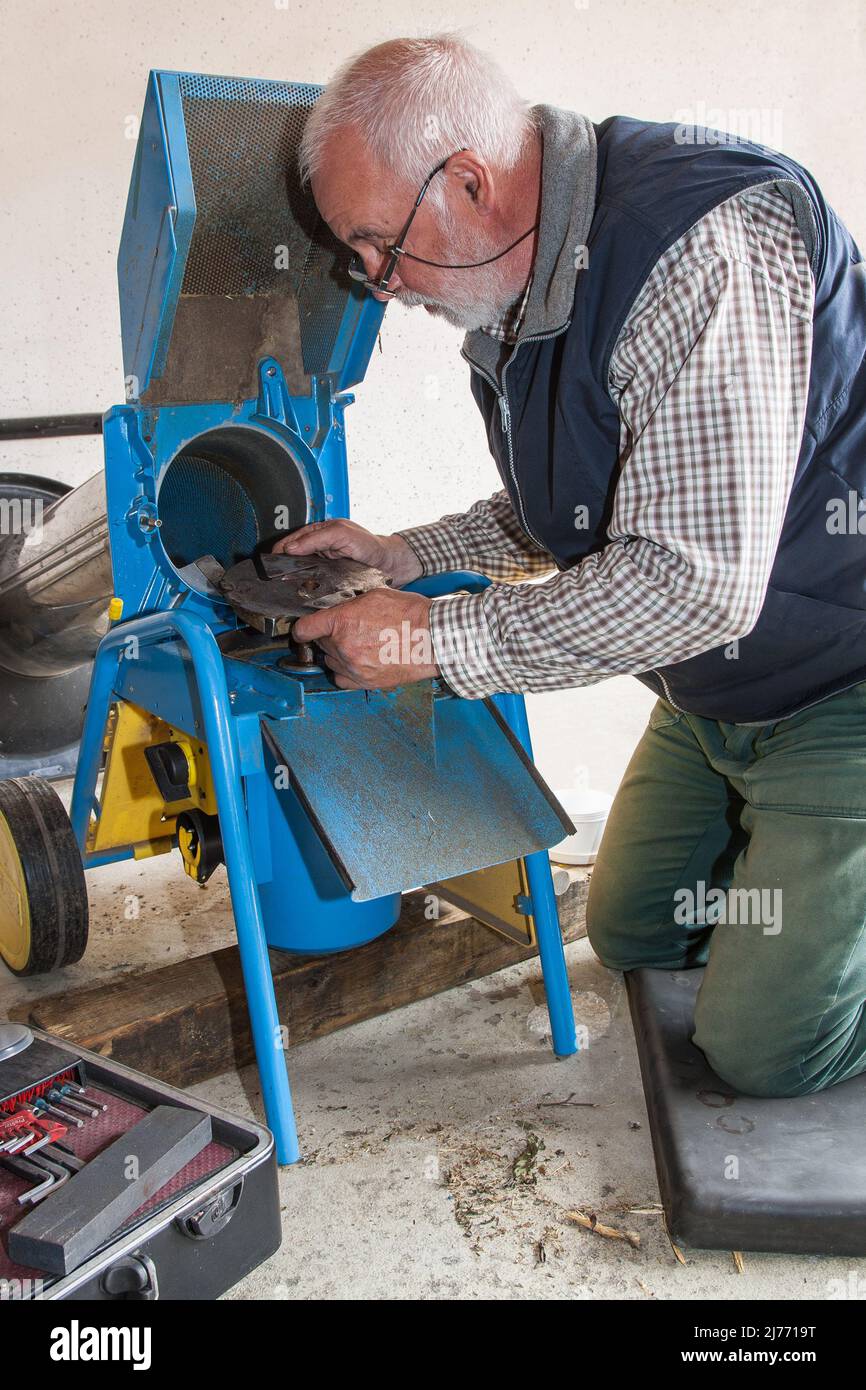 Il meccanico senior sta riparando un tritadocumenti da giardino presso il cliente e sta semplicemente mettendo in posizione la lama riparata. Foto Stock