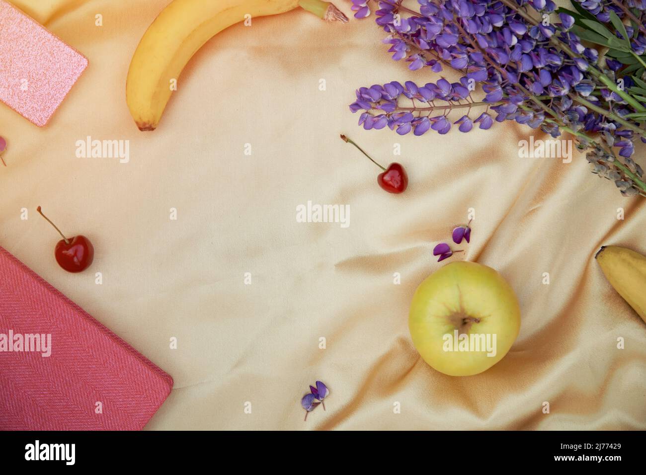 Lupini fiori viola, taccuino, mela, ciliegia banana decorazioni su sfondo dorato. Picnic estivo. Benessere vicinanza alla natura, auto-scoperta co Foto Stock