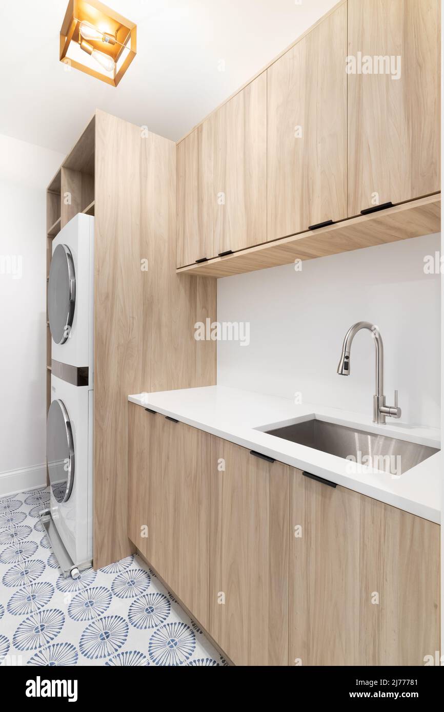 Una nuova sala lavanderia con armadi di legno, un ripiano in marmo bianco, pavimento in piastrelle a motivi geometrici, lavatrice e asciugatrice bianche e una lampada d'oro. Foto Stock