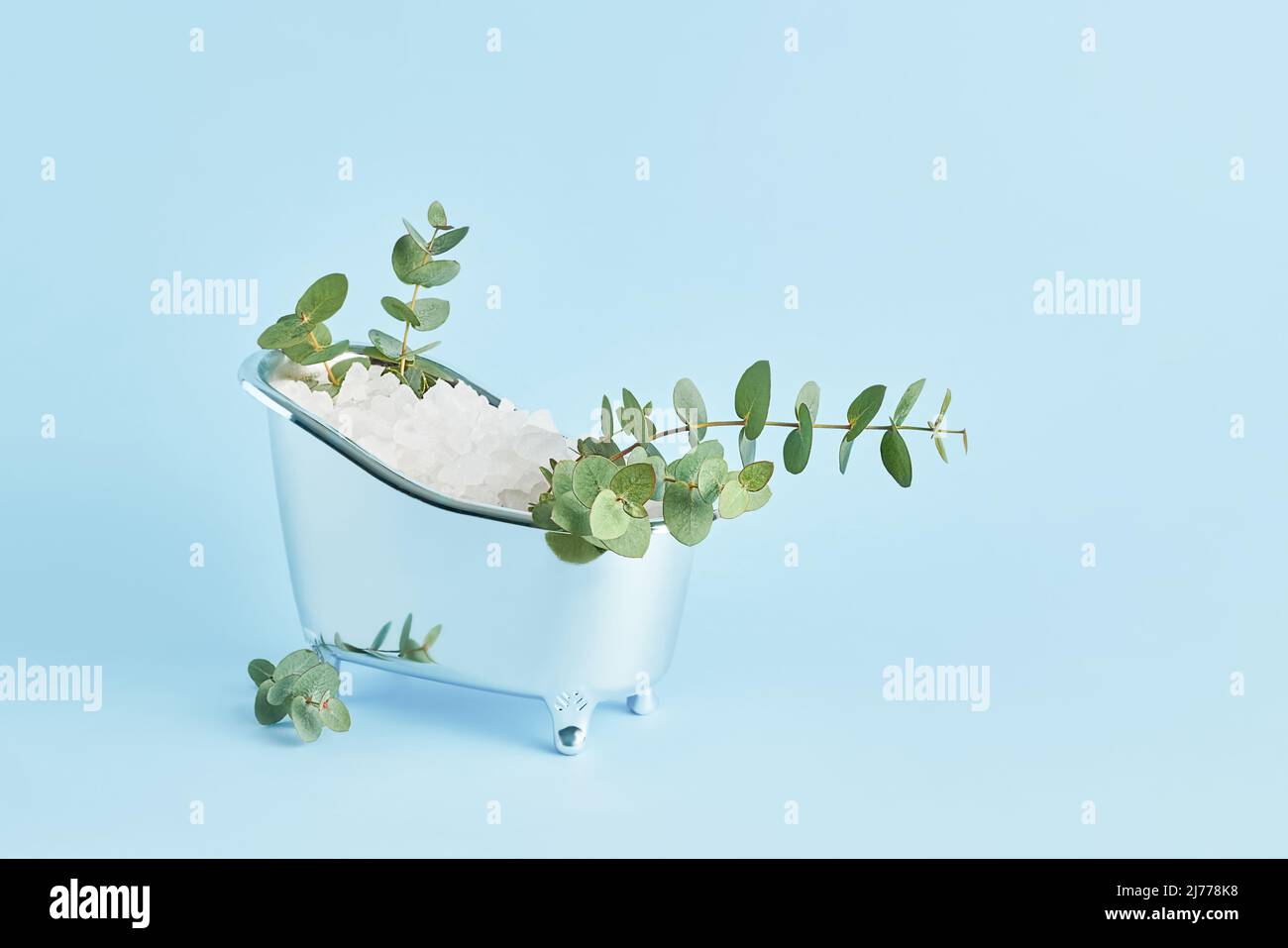 Bagno di sale bianco e rametti di eucalipto fresco in una piccola vasca da bagno su sfondo blu. SPA, concetto di cura del corpo. Spazio di copia per il testo Foto Stock