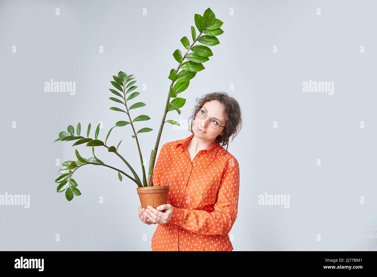Una donna vestita con abiti arancioni luminosi regge un vaso di fiori Foto Stock