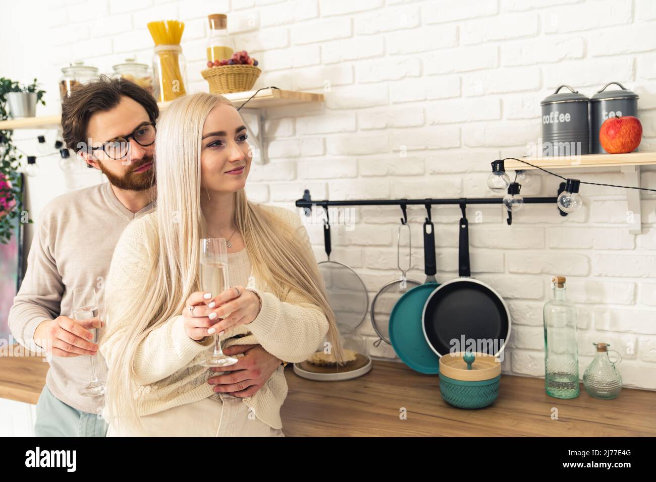 Concetto di anniversario. Uomo portico in occhiali e una donna bionda che abbraccia e beve vino bianco in una cucina ben attrezzata. . Foto di alta qualità Foto Stock