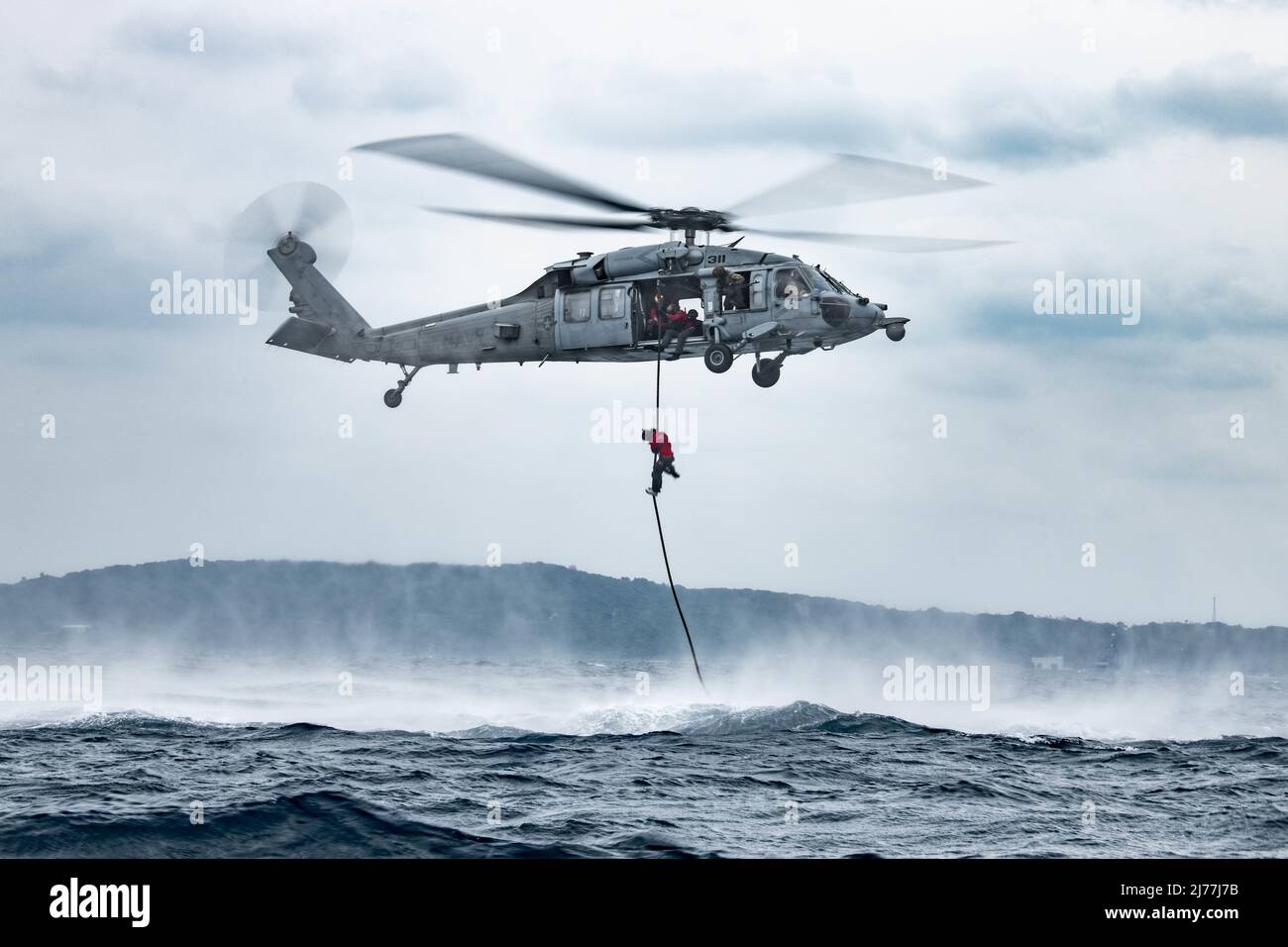 Un elicottero marino della marina degli Stati Uniti MH-60 Sea Hawk, assegnato a Helicopter Sea Combat Squadron 85, tira un pararescueman dell'aeronautica degli Stati Uniti, assegnato allo Squadrone speciale di tattica 320th, sopra l'acqua durante un addestramento alla struttura navale di White Beach, Giappone, 4 maggio 2022. Il team ha praticato il lancio di un'imbarcazione da combattimento in gomma da un elicottero marino MH-60 Sea Hawk degli Stati Uniti, saltando dopo di esso e assemblando il CRRC al momento dell'atterraggio in acqua. (STATI UNITI Air Force foto di Airman 1st Classe Sebastian Romawac) Foto Stock