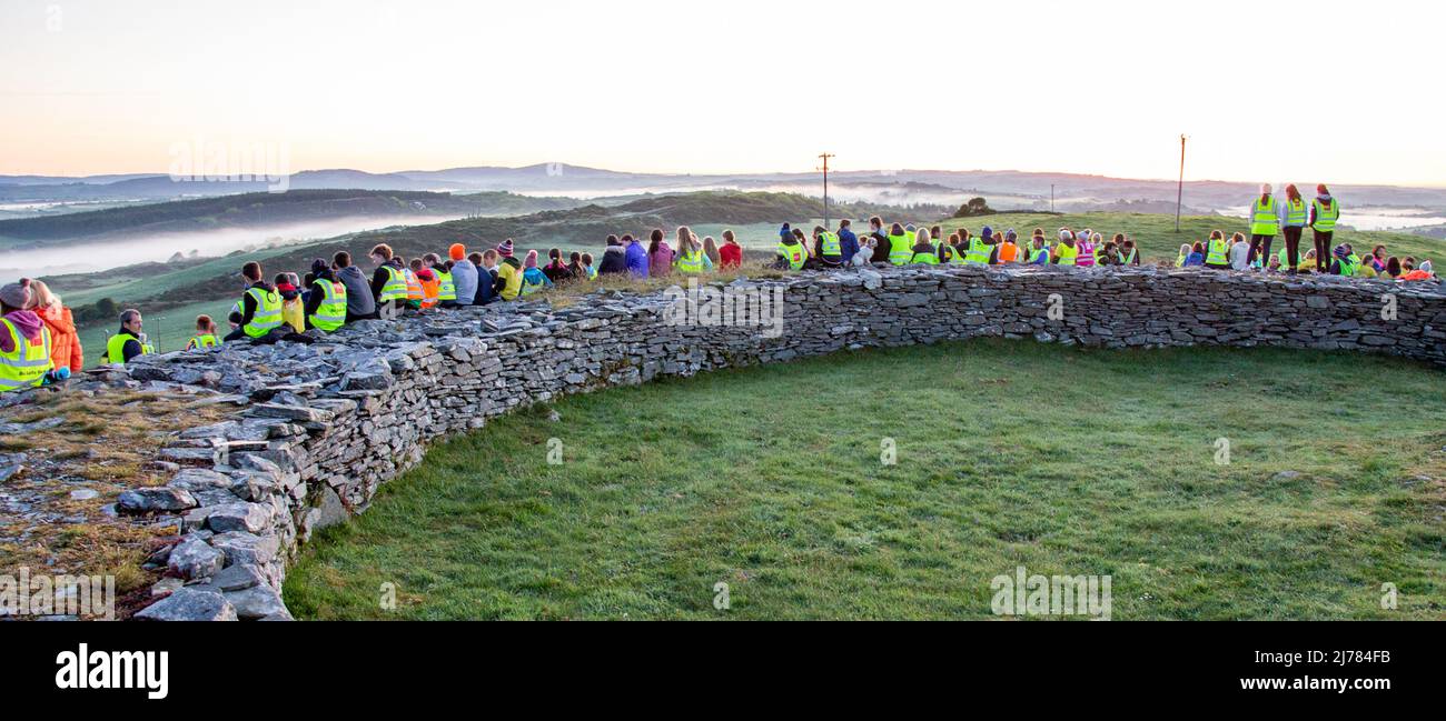 La folla che guarda l'alba sorgere del sole dopo l'oscurità nella luce cammina. Knockdrum pietra ring Fort, West Cork, Irlanda Foto Stock