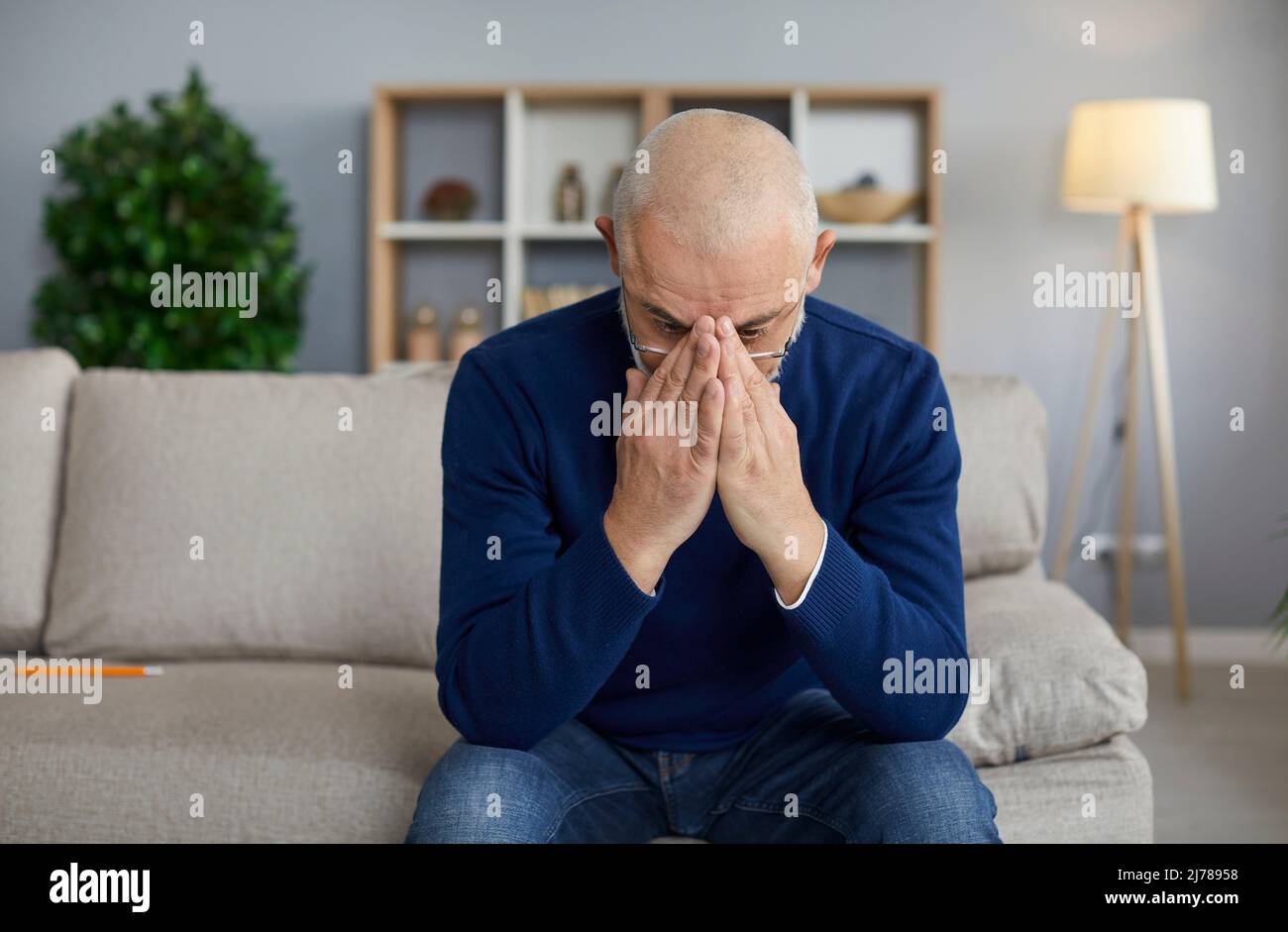 L'uomo anziano triste che sta addolorando per la perdita di sua moglie è seduto sul divano a casa Foto Stock