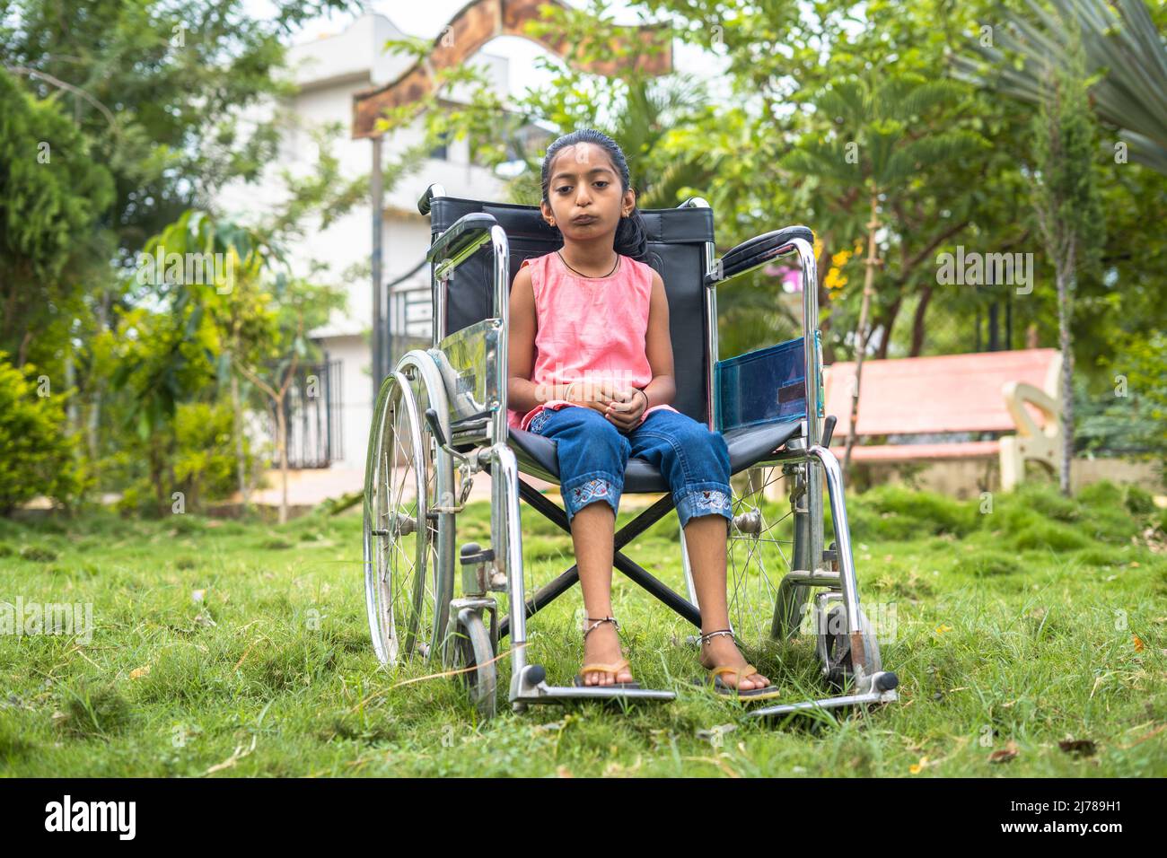Concetto di coraggio e motivazione che mostra con il bambino adolescente con disabilità utilizzando la sedia a rotelle guardando con sicurezza la macchina fotografica al parco. Foto Stock