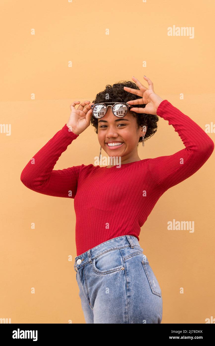 Una giovane donna latina in posa e sorridente davanti al muro arancione con occhiali da sole, Panama, America Centrale Foto Stock