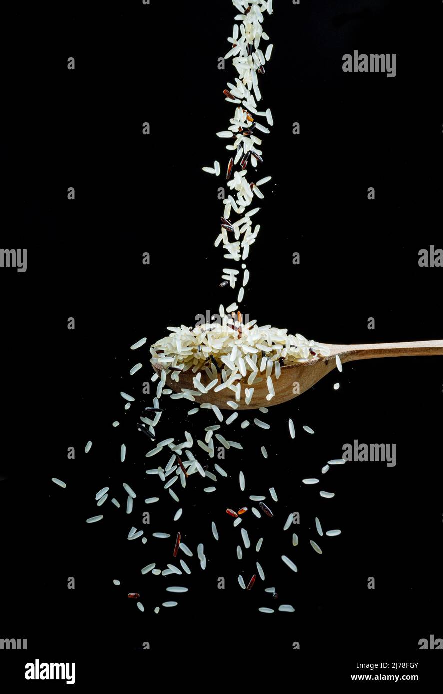 I grani di riso bianco cadono nel cucchiaio su sfondo nero. Cibo popolare e ingrediente principale di risotto e pilau. Foto Stock
