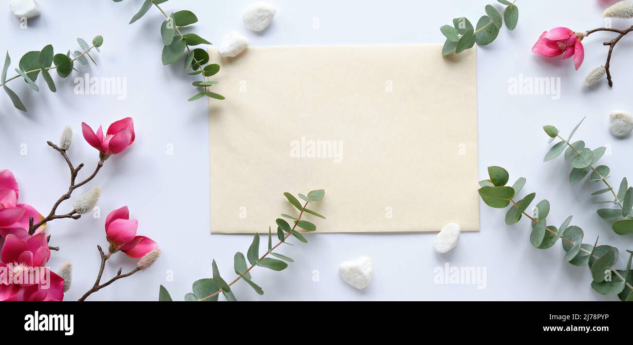 rosa magnolia fiori su rametti, foglie di eucalipto fresco. Cartoncino rosa vuoto con busta grigia. Foto Stock