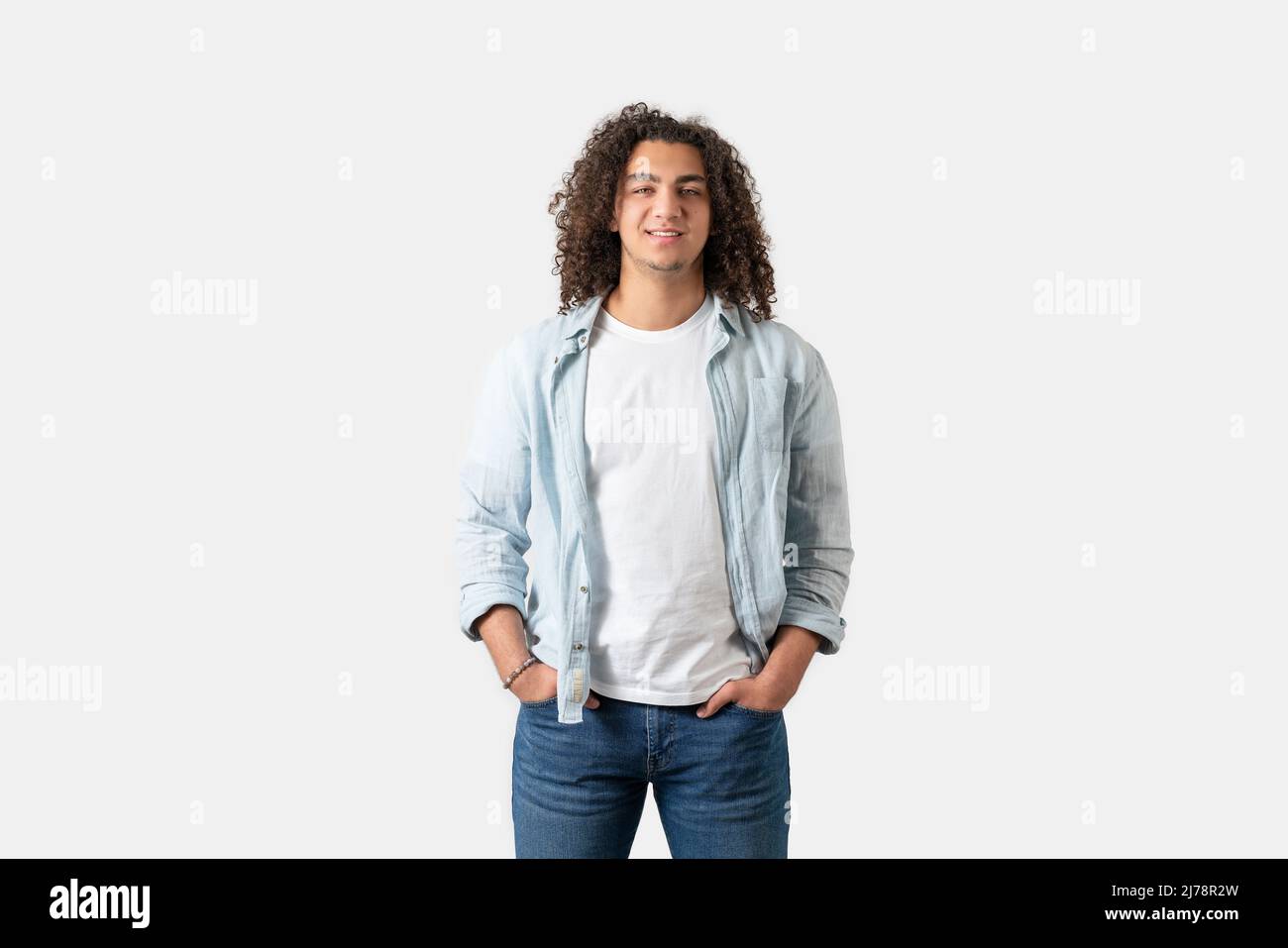 Primo piano di giovane uomo di buon aspetto con capelli lunghi e ricci sta posando, isolato su sfondo bianco. Foto di alta qualità Foto Stock