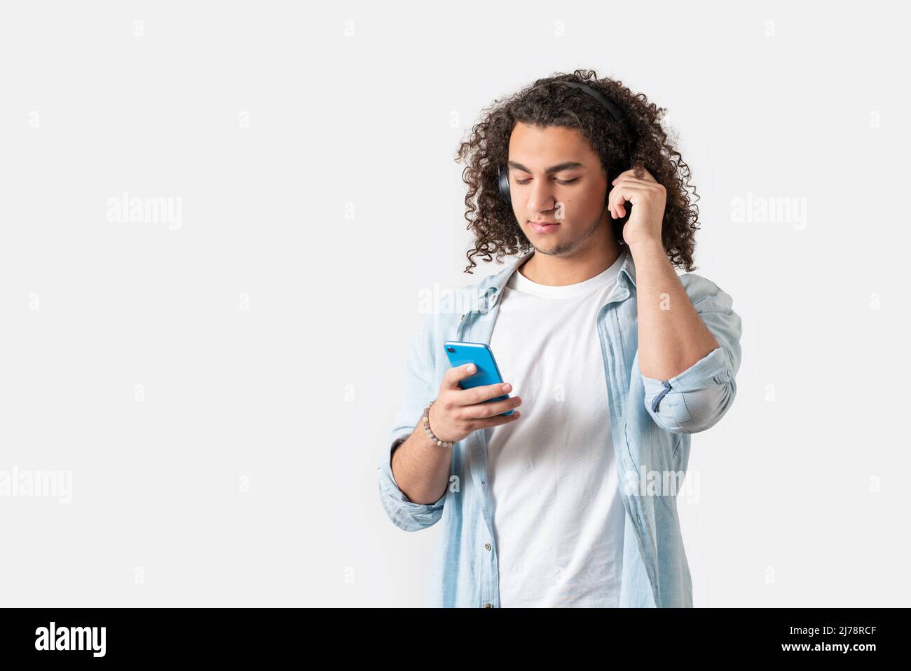 Giovane uomo di buon aspetto con cuffie che ascoltano la musica dal suo smartphone, isolato sfondo bianco. Foto di alta qualità Foto Stock