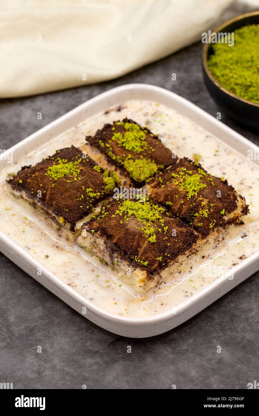 Baklava al cioccolato fondente. Baklava con latte su sfondo scuro. Prelibatezze della cucina mediterranea. Primo piano. Nome locale amaro baklava soguk Foto Stock