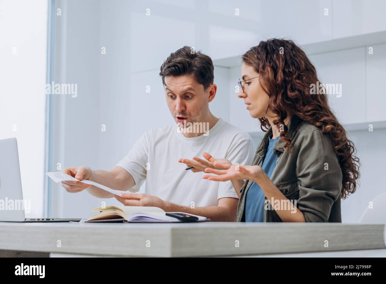 Coppia della moglie di brunette e del marito scuro-capelli che tiene il controllo del supermercato sostiene gesturing circa le spese non pianificate della famiglia dopo il calcolo Foto Stock