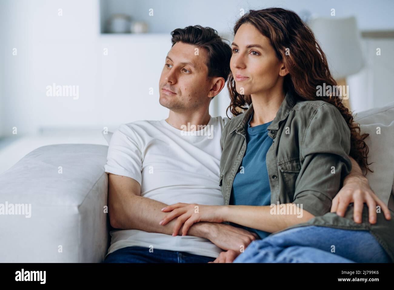 Sposi felici con capelli scuri sedersi su un comodo divano in soggiorno e discutere i piani per il futuro sorridendo ampiamente primo piano Foto Stock